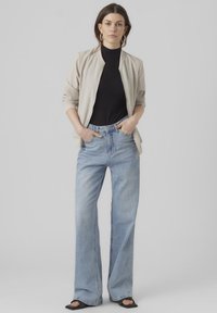 Light beige bomber jacket, black ribbed turtleneck, high-waisted light blue flared jeans, black open-toe heels, large hoop earrings.