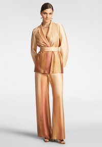 Completo in satin a due pezzi in tonalità degradé dal beige dorato a un morbido pesca, caratterizzato da un blazer avvolgente con cintura e pantaloni a gamba larga.