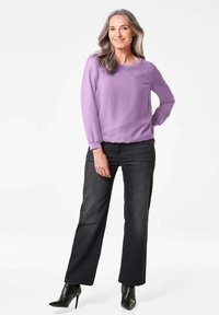 Lila langärmlige Bluse kombiniert mit dunklen Jeans im weit geschnittenen Stil und schwarzen High-Heel-Stiefeln. Weicher Stoff und lockere Passform.