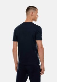 Marinblå t-shirt med kort ärm tillverkad av mjukt tyg. Har en klassisk rund hals och en avslappnad passform, synliga sömmar vid axlarna.