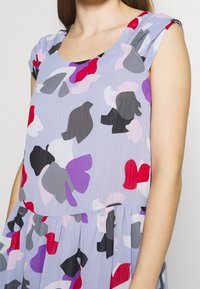 Kortärmad klänning i lätt tyg med en ljusblå bakgrund som har abstrakta mönster i röd, rosa, lila och svart.