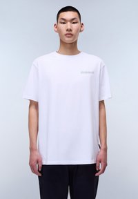 Camiseta blanca de algodón con cuello redondo, mangas cortas y un pequeño logo en el lado izquierdo del pecho. Diseño simple y sin adornos.