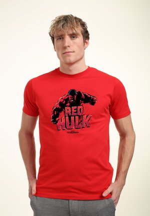 Czerwona bawełniana koszulka z nadrukiem przedstawiającym muskularną postać z napisem "CZERWONY HULK". Krótkie rękawy i klasyczny krój z okrągłym dekoltem.