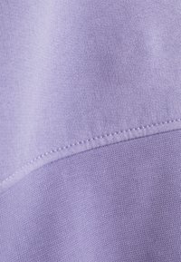 Tejido púrpura claro con una textura suave. Presenta costuras visibles a lo largo de la unión, lo que resalta un diseño simple y limpio.