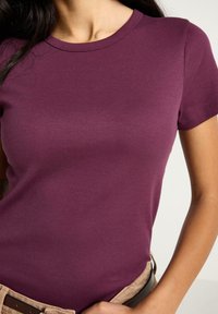 T-shirt a maniche corte con scollo rotondo in lavanda, realizzata in tessuto costina, con vestibilità attillata e tessitura liscia. Cintura visibile in vita.