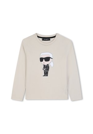 Beige shirt met lange mouwen met een cartoonfiguur op de voorkant die een zonnebril draagt, een zwart jack en wit haar in een paardenstaart.