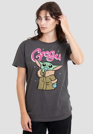Graues Baumwoll-T-Shirt mit einer Cartoonfigur mit großen Ohren und grüner Haut, die einen Snack hält. Das Design enthält pinken Text: "Grogu."