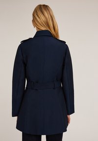 Granatowa kurtka z paskiem w talii, dopasowanym kroju i pagonami na ramionach. Gładka tekstura i dopasowana sylwetka.