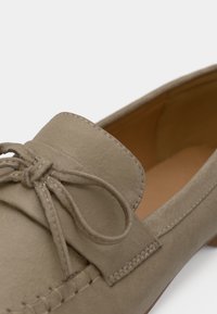 Ταουπ μοκασίνι από δέρμα με ραμμένες λεπτομέρειες και δεμένο φιόγκο στο μπροστινό μέρος, που δείχνει την εσωτερική επένδυση σε αποχρώσεις του ταμπά.