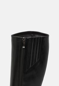 Czarne buty z ekoskóry z zamkiem błyskawicznym, z pionowymi żebrowanymi akcentami po bokach i gładką fakturą.