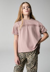 Rosenpink kortærmet T-shirt med et struktureret loop-design over brystet, parret med mønstrede leopardprint bukser i sort og tan farver.