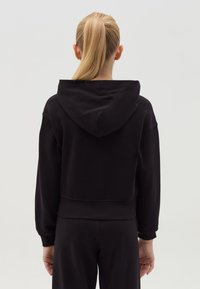Sudadera corta negra de tejido suave, con capucha ajustable, puños acanalados y un corte relajado. Textura suave y diseño minimalista.
