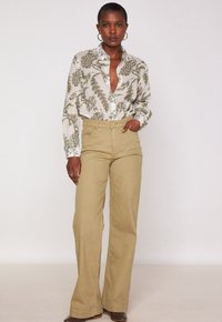 Camicia a bottone con stampa botanica verde, abbinata a pantaloni beige a gamba larga. Caratteristiche includono un colletto e tasche frontali.