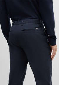 Navy blue trousers with a textured fabric, belt loops, and two back pockets. Features a small white "BOSS" logo on the right pocket.