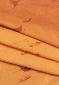 Tessuto arancione con una consistenza morbida, piegato con un motivo sottile in tonalità più scure. Il materiale appare leggero e liscio.
