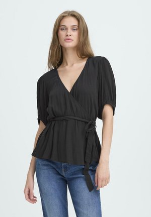 Zwart wikkelblouse met een diepe V-hals, poffende mouwen en een ceintuur om de taille. Zachte, gestructureerde stof met een vloeiende vorm. gedragen met blauwe spijkerbroek.