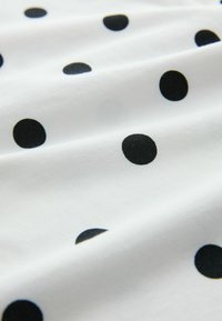 Biała tkanina w czarne kropki, o miękkiej fakturze i gładkim układzie. Kropki różnią się rozmiarem, tworząc wzorowany design.