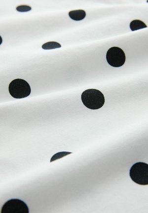 White fabric with black polka dots, featuring a soft texture and smooth draping. Dots vary in size, creating a patterned design.
