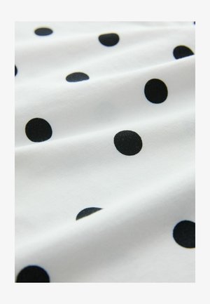 Weißer Stoff mit schwarzen Punkten, der eine weiche Textur und fließende Drapierung aufweist. Die Punkte variieren in der Größe und erzeugen ein gemustertes Design.