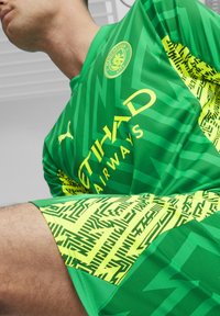 Zöld mez sárga kiegészítőkkel, cikk-cakk mintázattal és logókkal. A nadrág zöld, geometrikus sárga mintázattal. Lélegző anyagból készült.