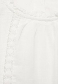 Weiße Bluse aus strukturiertem Baumwollstoff mit Volantkragen und aufwändiger floralem Stickerei entlang der vorderen Naht.