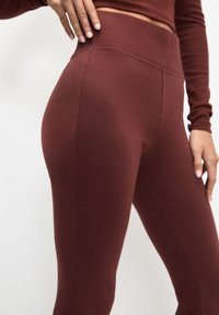 Bordowe legginsy z wysokim stanem o gładkiej fakturze, z szerokim pasem i dopasowanym krojem, podkreślające smukłą sylwetkę.