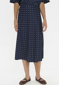 Jupe midi à pois navy en tissu lisse, dotée de pois blancs, d'une taille ajustée et d'une silhouette fluide. Des chaussures plates marron sont visibles.