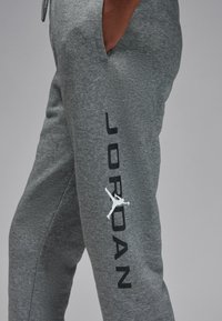 Hallid fliisist püksid musta "JORDAN" tekstiga ja valge Jumpmani logoga vasakul jalal. Omavad küljetaskuid ja lõdva sobivusega disaini.