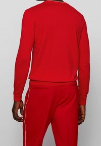 Maglia rossa a maniche lunghe e pantaloni abbinati, con texture a costine, vestibilità slim, collo rotondo e tasche laterali, rifiniti con dettagli in piping bianco.