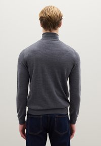 Maglione grigio a collo alto con maniche lunghe e polsini a coste, abbinato a jeans blu scuro. Tessuto liscio, design aderente. Vista posteriore.