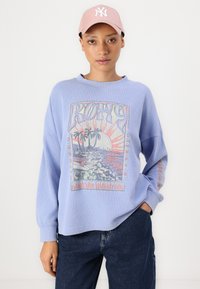 Lichtblauwe sweatshirt met een grafische print van palmbomen en een zonsondergang, gecombineerd met een roze baseballcap. Casual, ontspannen pasvorm ontwerp.