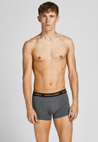 Donkergrijze boxershorts met een elastische tailleband met oranje tekst. De stof lijkt glad en rekbaar, ontworpen voor comfort.