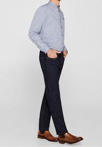 Camicetta azzurra chiara con colletto a camicia, jeans in denim scuro e stivali alla caviglia in pelle marrone con pannelli elasticizzati laterali.