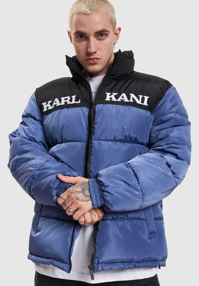 Mėlynas ir juodas pūkinis švarkas su paminkštinta išore, aukštu apykakle, zip uždarymu ir spaudiniais "KARL" ir "KANI" ant krūtinės.