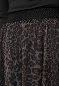 Gonna a stampa leopardata con una texture trasparente, caratterizzata da una fascia elastica nera in vita e un design plissettato. Il motivo presenta accenti marrone scuro e neri.
