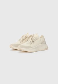 Baskets de sport beiges avec un dessus texturé, des lacets plats et une semelle rembourrée. Les détails d'accent incluent un embout en beige clair et un logo.