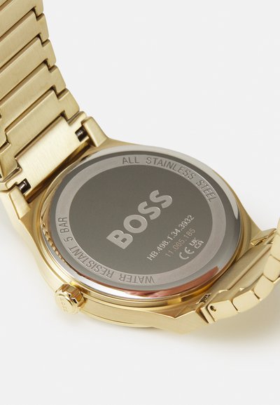 Montre en acier inoxydable doré à l'arrière présentant une surface lisse et le logo "BOSS" gravé ; étanche jusqu'à 5 bars.