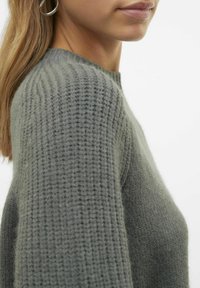 Maglione grigio a maglia con texture a costine, scollo rotondo e vestibilità comoda. Il materiale sembra morbido e leggermente peloso.