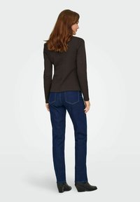 Langsleeve, aansluitend donkerbruine top gecombineerd met donkerblauwe denim jeans. Gladde textuur met stikseldetails en zwarte haklaarzen.