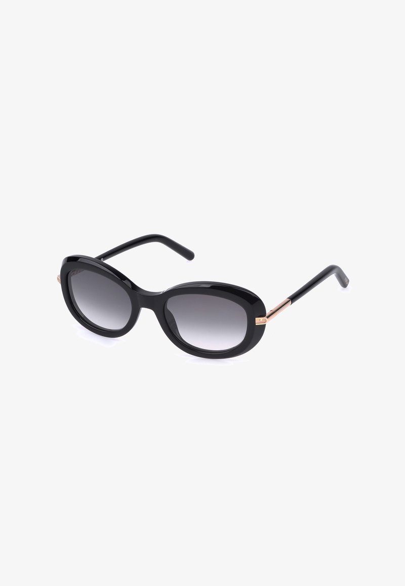 Lunettes de soleil ovales noires avec des verres à dégradé foncé et des branches fines soulignées de doré, posées sur un fond blanc.
