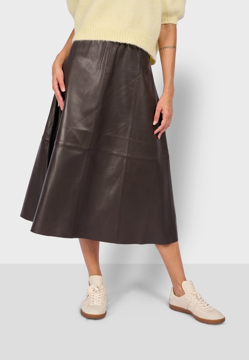 Jupe midi en cuir marron avec un design évasé, dotée de surpiqûres et d'une taille élastique, associée à des baskets blanches.