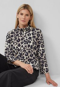 Top leopard print in crema con macchie nere, caratterizzato da un colletto alto e maniche a tre quarti, realizzato in un tessuto morbido.