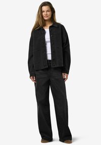 Svart denimjakke med knappelukking og to frontlommer, kombinert med matchende svarte vide jeans. Hvit t-skjorte under.