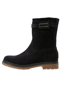 Svart mocka ankelsko med en sömdesign, gummisula och ett dekorativt band med en guldfärgad spänne högst upp.