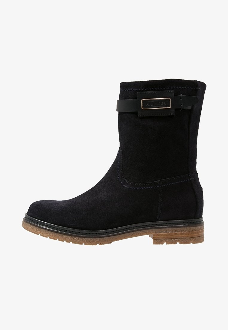 Svart mocka ankelsko med en sömdesign, gummisula och ett dekorativt band med en guldfärgad spänne högst upp.