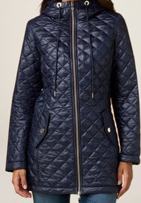 Abrigo acolchado azul marino con cierre de cremallera, capucha con cordón, dos bolsillos laterales y acentos metálicos. Presenta una textura suave y brillante.