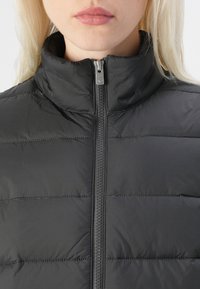 Čierny puff vest s vysokým golierom, s vodorovným prešívaním, plným zipsom vpredu a hladkým, lesklým povrchom.