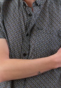 Korte mouwen shirt van zwarte stof met een blauw-wit ruitpatroon, voorzien van zwarte knopen en een klein logo op de borstzak.