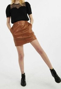 Svart topp med genomskinlig prickig overlay, i kombination med en brun fusk läderkjol med knappar fram och sidofickor. Svarta ankelskor.