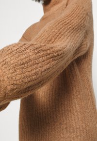Maglione a coste marrone con una superficie testurizzata, colletto alto e vestibilità morbida. Tessuto morbido con leggere sfumature in tutta la trama.